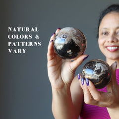 female model holding two brown opal spheres showing natural colors and patterns vary